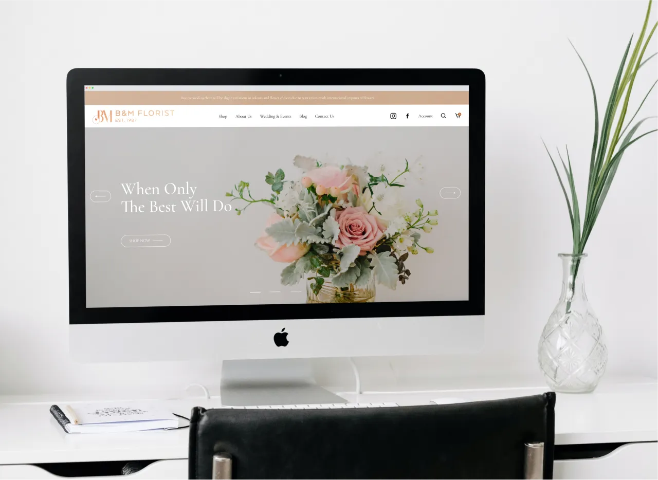 An iMac on a white desk beside a vase of grass, showing the B&M Florist home page, a pastel bouquet under the headline "When Only The Best Will Do".